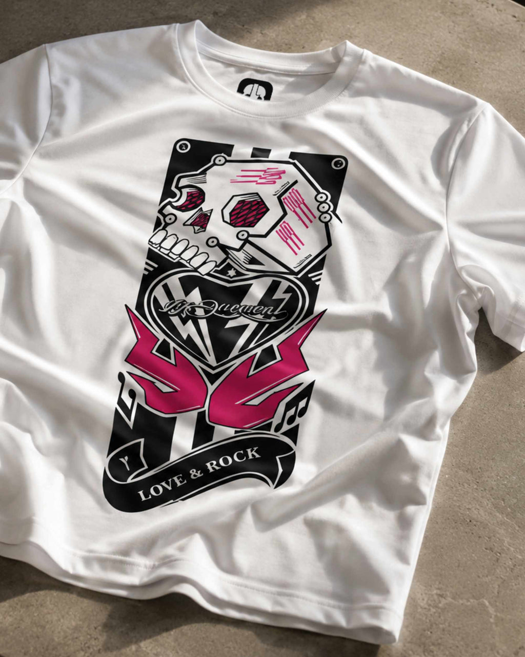 A white short-sleeve t-shirt laid flat on a textured concrete floor, featuring a large graphic print on the front with a skull, pink stylized '55' text, and the words 'LOVE & ROCK'.