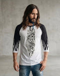 Man wearing a white and black three-quarter sleeve raglan shirt featuring the Sakura Revolution artwork with a skull, flowers, and flowing ornamental details.
