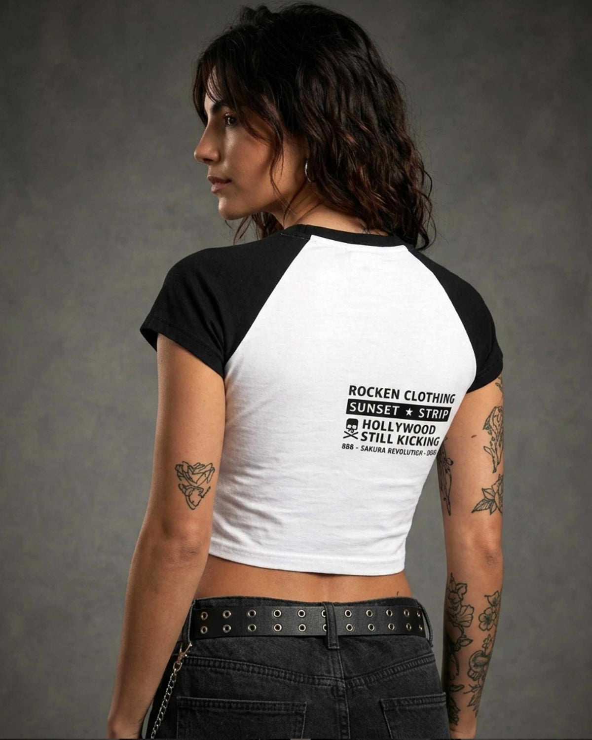Back view of a woman wearing a black and white cropped raglan shirt with a small ROCKEN graphic and typography printed on the upper back.