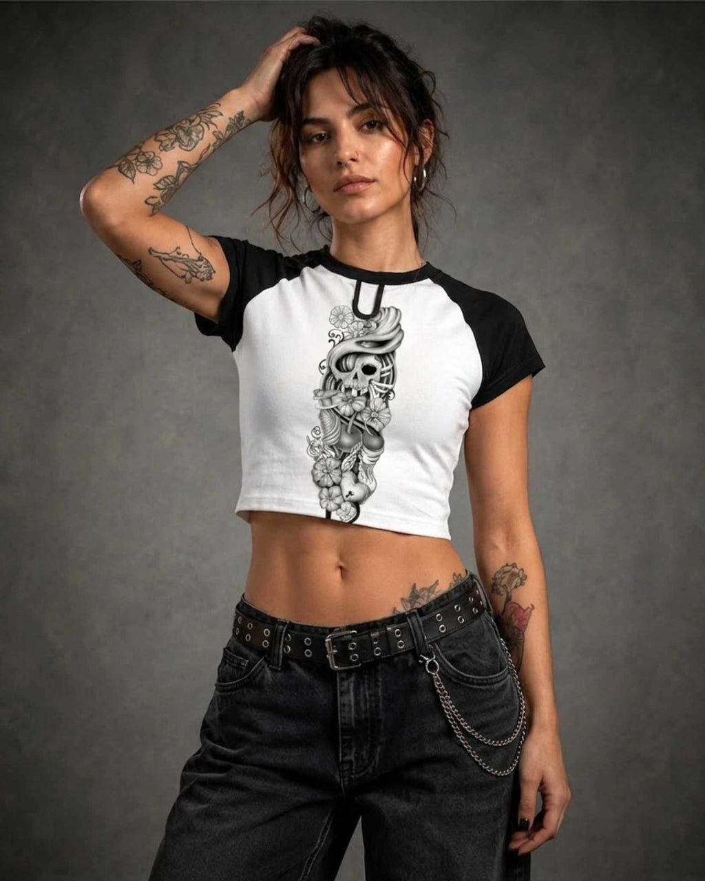 Woman wearing a black and white cropped raglan shirt featuring the Sakura Revolution artwork with a skull, flowers, and flowing ornamental details.
