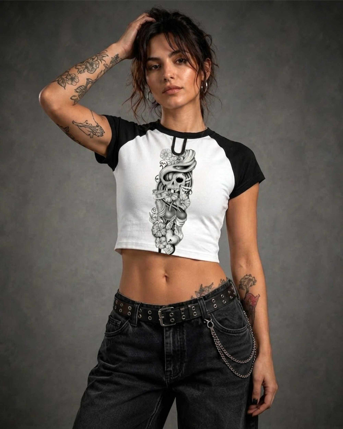 Woman wearing a black and white cropped raglan shirt featuring the Sakura Revolution artwork with a skull, flowers, and flowing ornamental details.