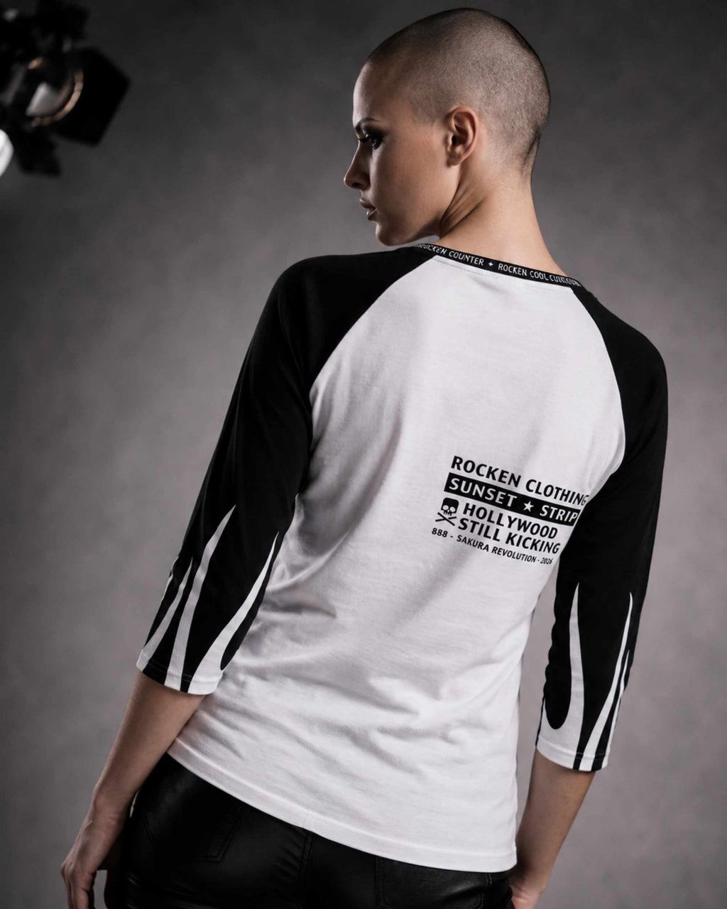 Close-up of the back of a woman wearing a white and black three-quarter sleeve raglan shirt with a ROCKEN graphic and typography printed on the upper back.