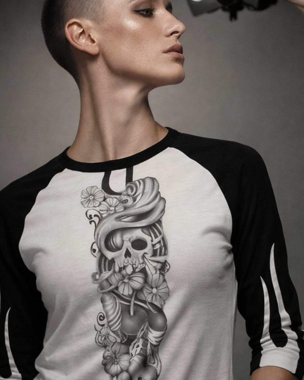 Close-up of a woman wearing a white and black three-quarter sleeve raglan shirt featuring the Sakura Revolution artwork with a skull, flowers, and flowing ornamental details.