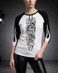 Close-up of a woman wearing a white and black three-quarter sleeve raglan shirt featuring the Sakura Revolution artwork with a skull, flowers, and flowing ornamental details.